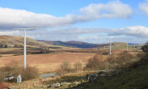 An overview of Lake Bala under a cloudy blue sky with electricity masts extending into the background 
