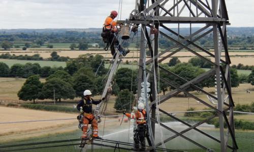 Engineers wearing PPE climbing up an electricity tower and along the overhead lines