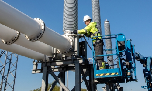 Engineer wearing PPE working from a cherry-picker on electricity switchgear at a substation