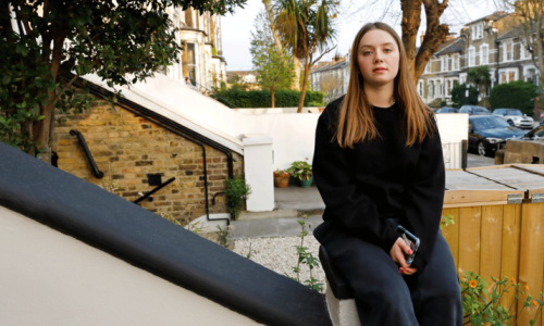 Young woman with long hair sitting on the banister of a house in an urban street