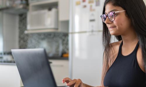 Young woman at kitchen table working on laptop for National Grid virtual interview skills story