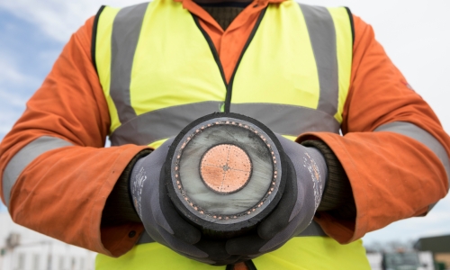Close up of a person wearing orange overall and high-vis vest holding a section of an interconnector cable