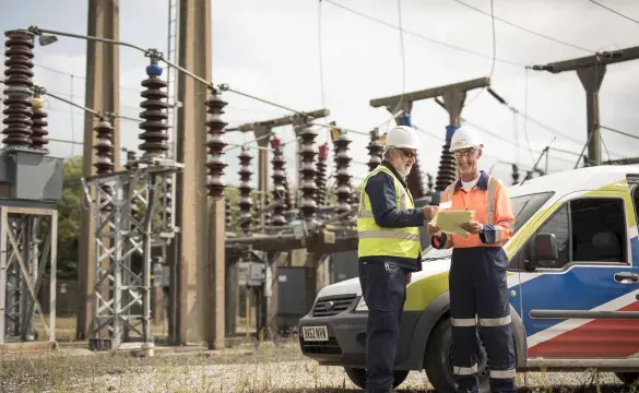 Two National Grid employees standing in front of an electricity plant and a National Grid vehicle 