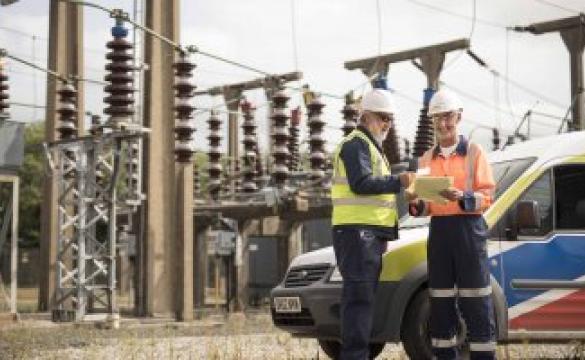 Two National Grid employees standing in front of an electricity plant and a National Grid vehicle