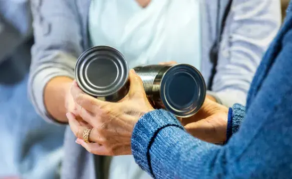 Woman passing two food tins to another person - used for the National Grid story 'Making a difference during the coronavirus outbreak'