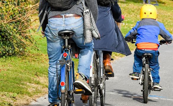 Two adults and a child wearing a yellow helmet cycling on path