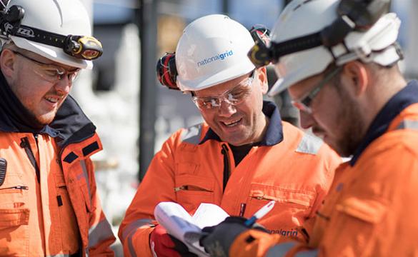 Three National Grid construction engineers wearing hard hats and PPE discussing paperwork