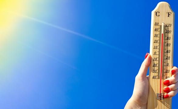 Hand holding thermometer showing high temperatures in the sun