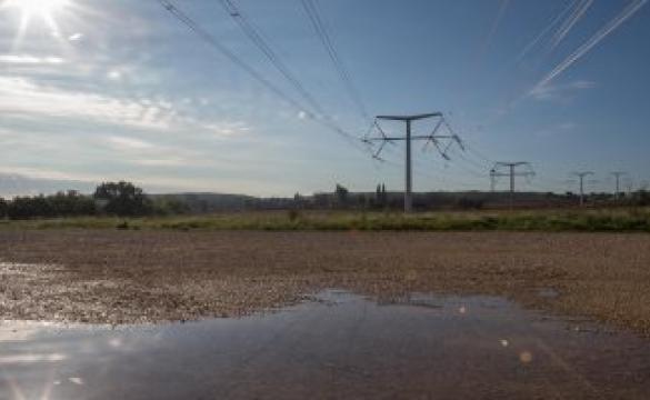 A muddied wet patch of land with grass and electricity structures stretching into the background