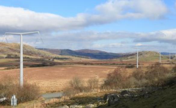 An overview of Lake Bala under a cloudy blue sky with electricity masts extending into the background