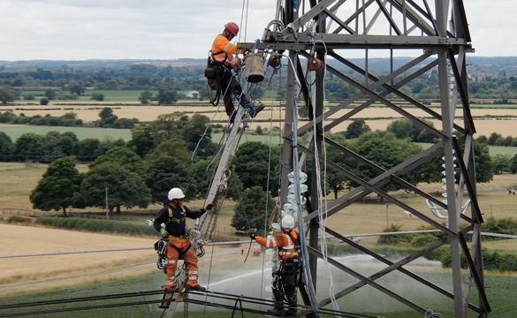 Engineers wearing PPE climbing up an electricity tower and along the overhead lines