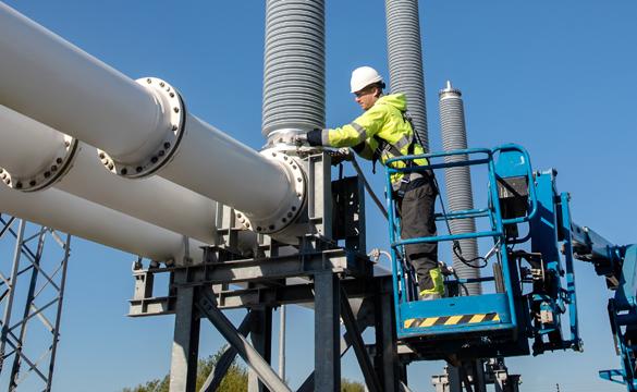 Engineer wearing PPE working from a cherry-picker on electricity switchgear at a substation