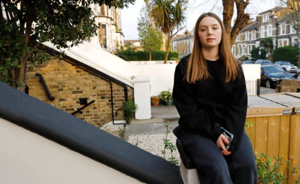 Young woman with long hair sitting on the banister of a house in an urban street