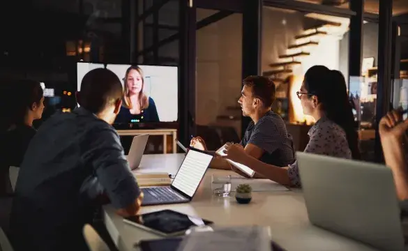 A group of individuals sitting around a table in front of a conference call screen