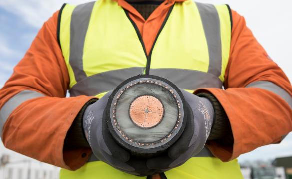 Close up of a person wearing orange overall and high-vis vest holding a section of an interconnector cable