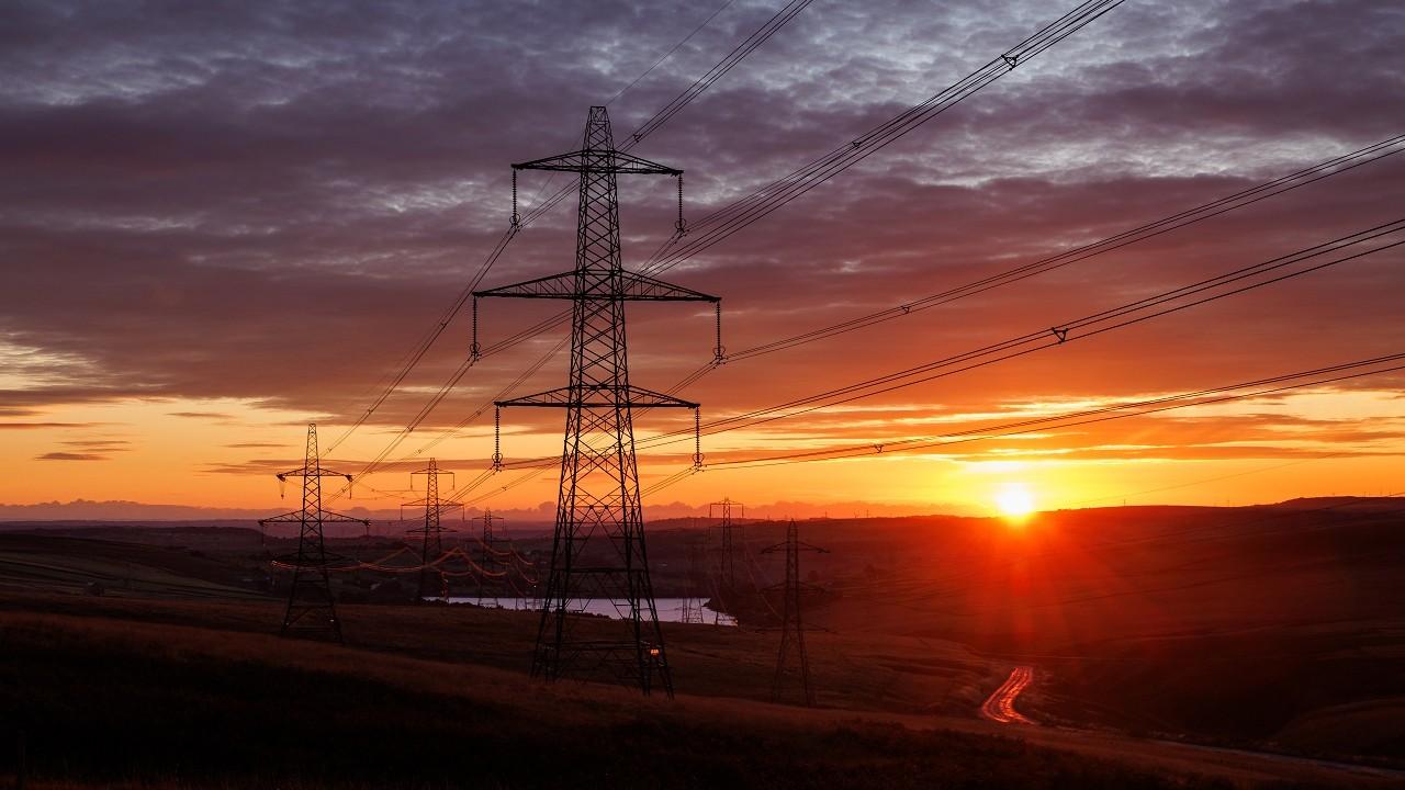 Row of electricity pylons and overhead lines at sunset