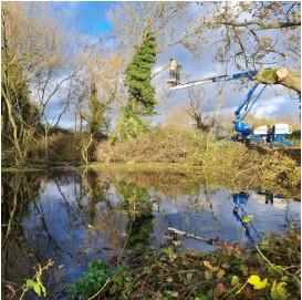 Vegetation management worker in bucket truck with pond