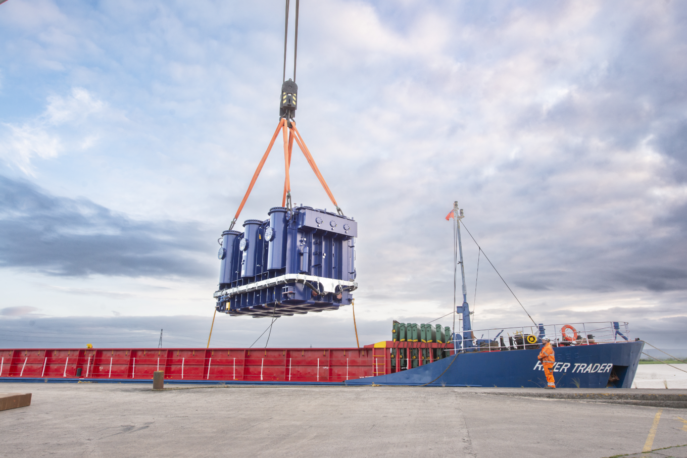 Photograph of a supergrid transformer being delivered at a port. The transformer is attached to a crane, which is transporting the transformer off a boat.