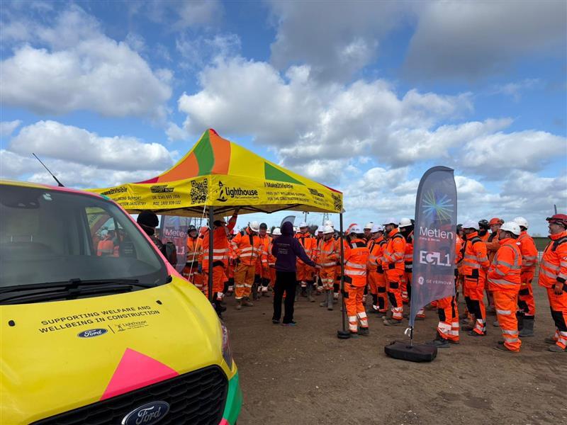 People in Orange Construction Gear Standing Near Pop Up Tent