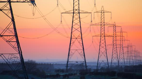 Row of lattice electricity pylons against an orange sky