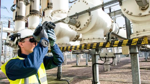 Man wearing PPE using camera to detect SF6 leaks at substation