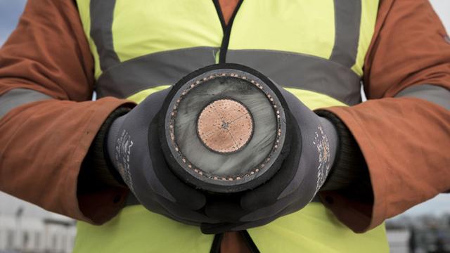 Person wearing a high-vis vest and safety gloves holding a sample of an interconnector cable