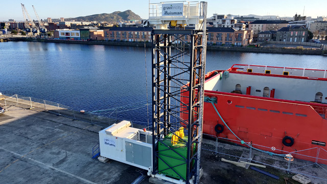 Gravity energy storage tower at a dock beside a red ship
