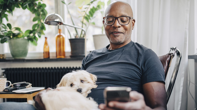 Smiling retired senior male using smart phone with dog on his lap