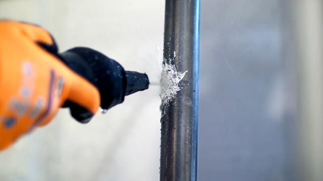 A gloved hand holding a drill, drilling into a metal pipe