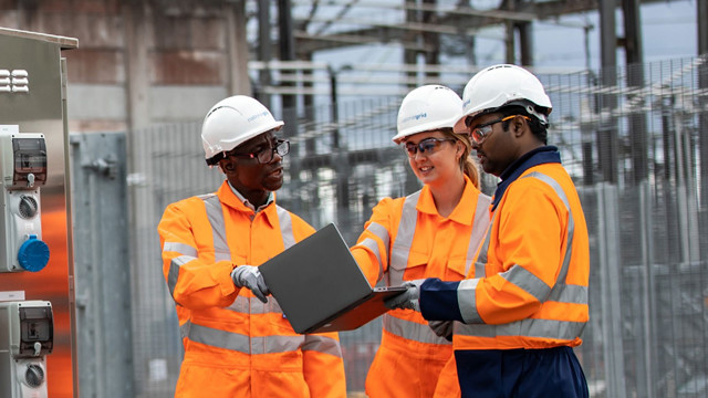 Three National Grid engineers wearing full PPE looking at a laptop at a substation