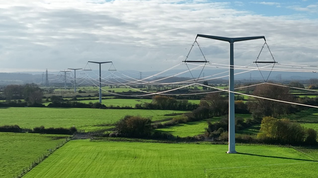 Electricity overhead lines running between T-pylons in green fields