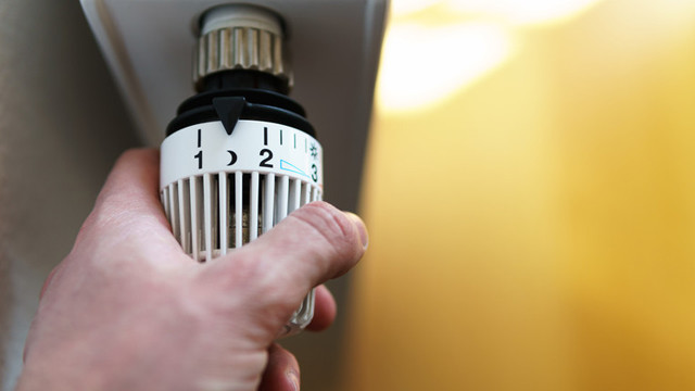 A hand turning down a radiator thermostat valve
