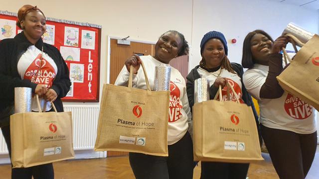 Four smiling women holding Plasma of Hope tote bags with winter warmth kits