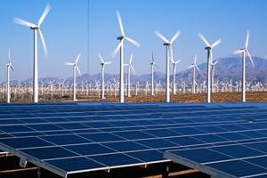 Solar panels and wind turbines in a field with mountains in the background