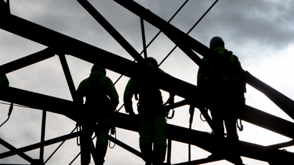 A silhouette of four individuals against an industrial structure with grey clouds in the background 