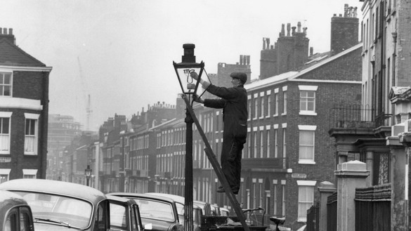 Early century black and white photo of man lighting street light for National Grid history