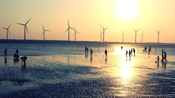 Silhouettes of people on a beach at sunset with wind turbines out at sea in the background
