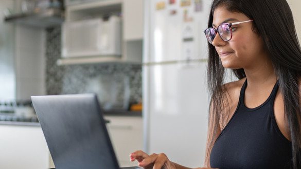 Young woman at kitchen table working on laptop for National Grid virtual interview skills story