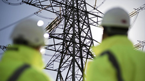 Two people wearing high-vis jackets and hard hats standing in front of electricity pylon