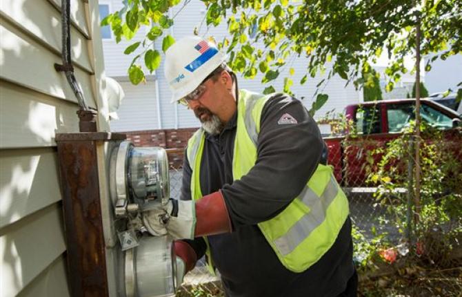 National Grid employee working on a system box fixed to the side of a building with trees and a car in the background 