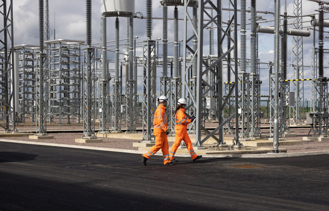 Two engineers wearing orange overalls and PPE in the Viking Link converter station AC yard