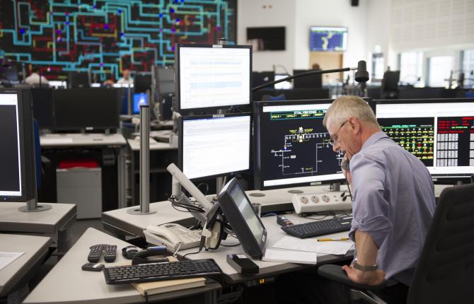 National Grid employee on the phone at a desk in front of many computer screens with an office in the background
