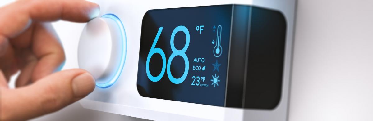 A person's hand adjusts a digital thermostat