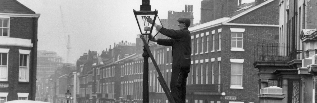 Early century black and white photo of man lighting street light for National Grid history