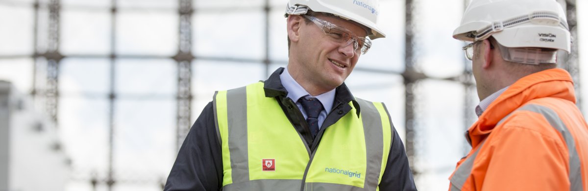 An image of National Grid CEO John Pettigrew and another man in safety gear in front of a gas holder