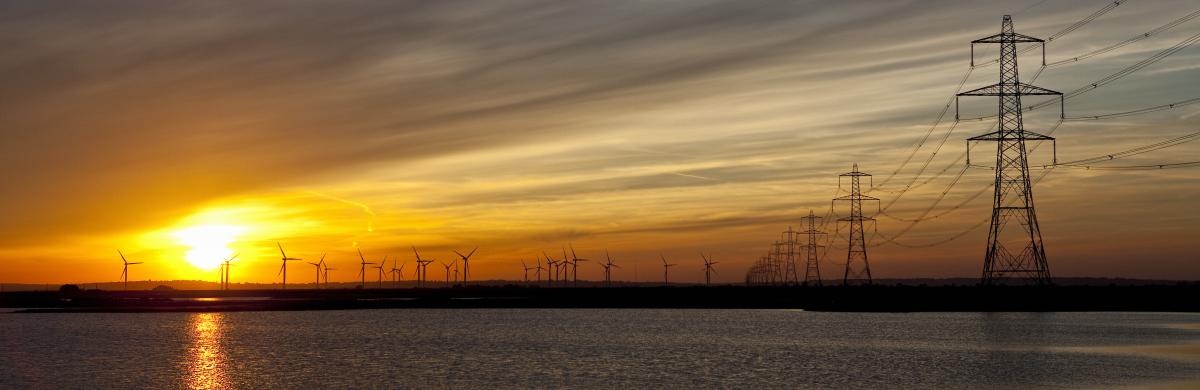 A beach at sunset with the sea coming in and electricity pylons dotted into the distance 