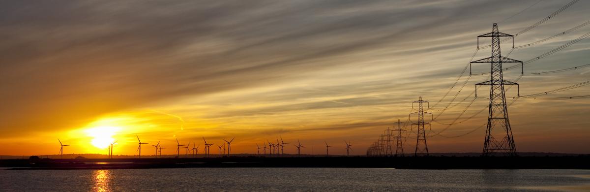 A beach at sunset with the sea coming in and electricity pylons dotted into the distance 