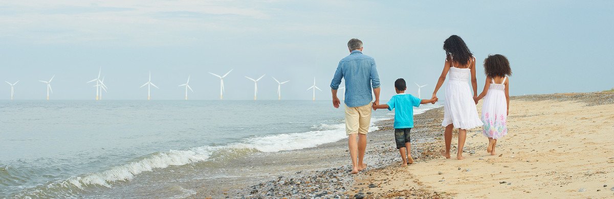 Family holding hands as they walk along a sandy beach with wind turbines in the background