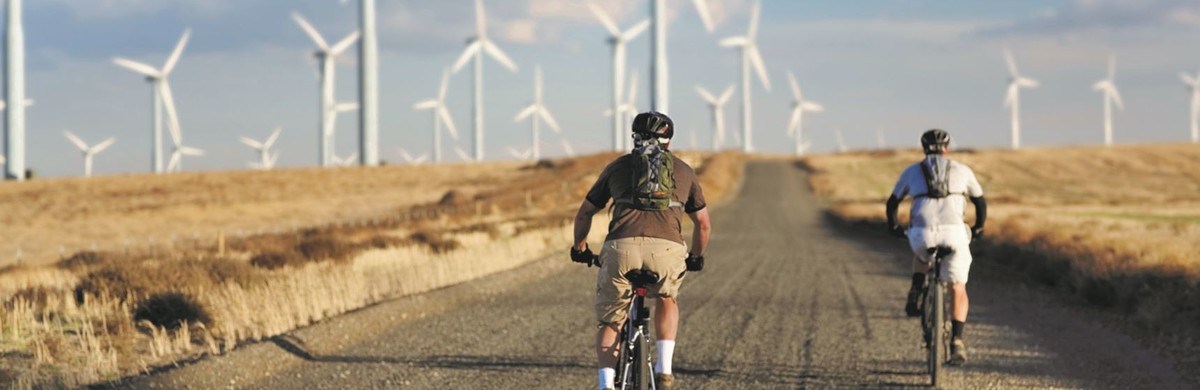 2 men cycling by some wind turbines