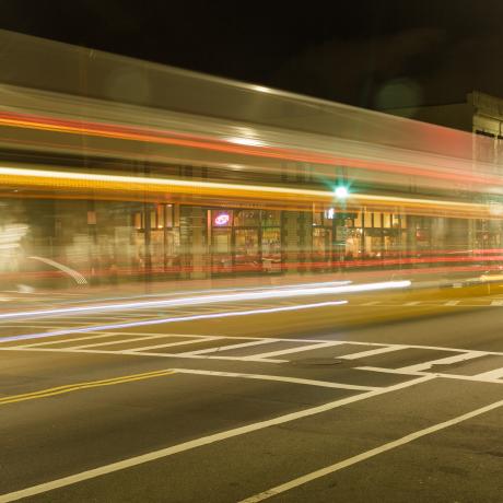 A street-view that it well-lit at night-time with driving cars out of focus